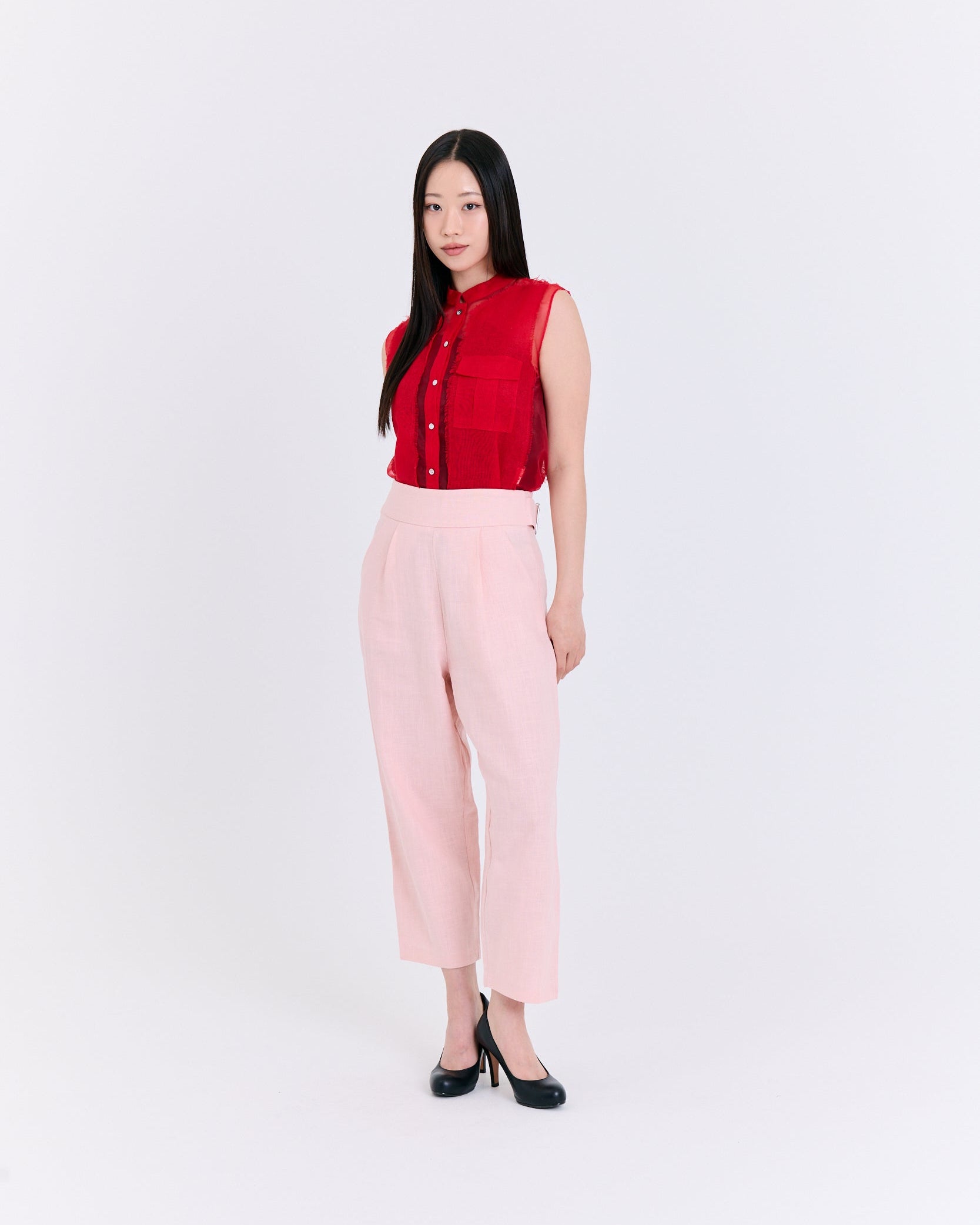 Woman wearing a red sleeveless blouse and pink pants on a white background