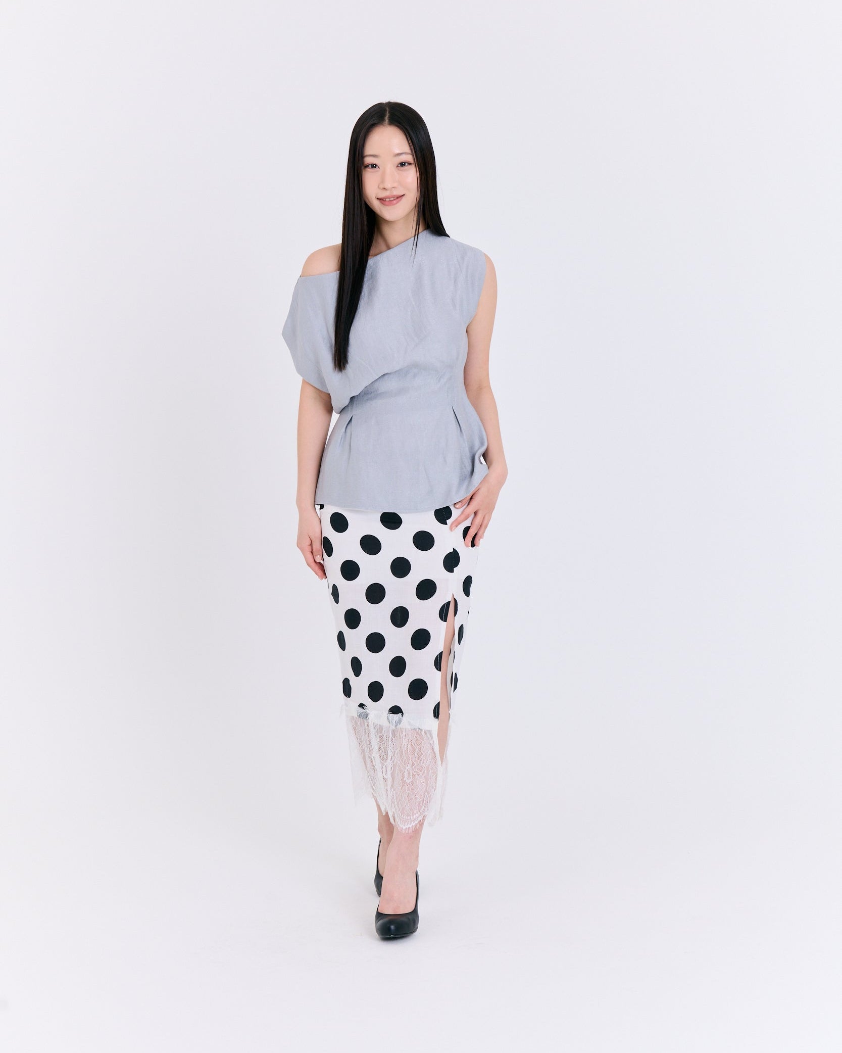 Woman wearing a gray off-shoulder top and black and white polka dot skirt on a white background