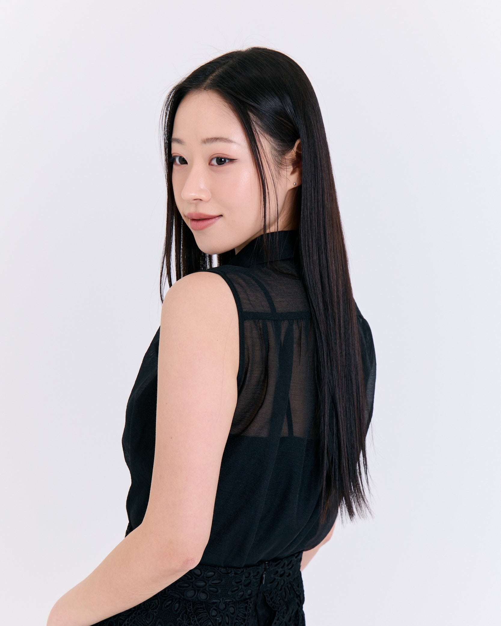 Woman wearing a black sleeveless top with sheer panels on a white background