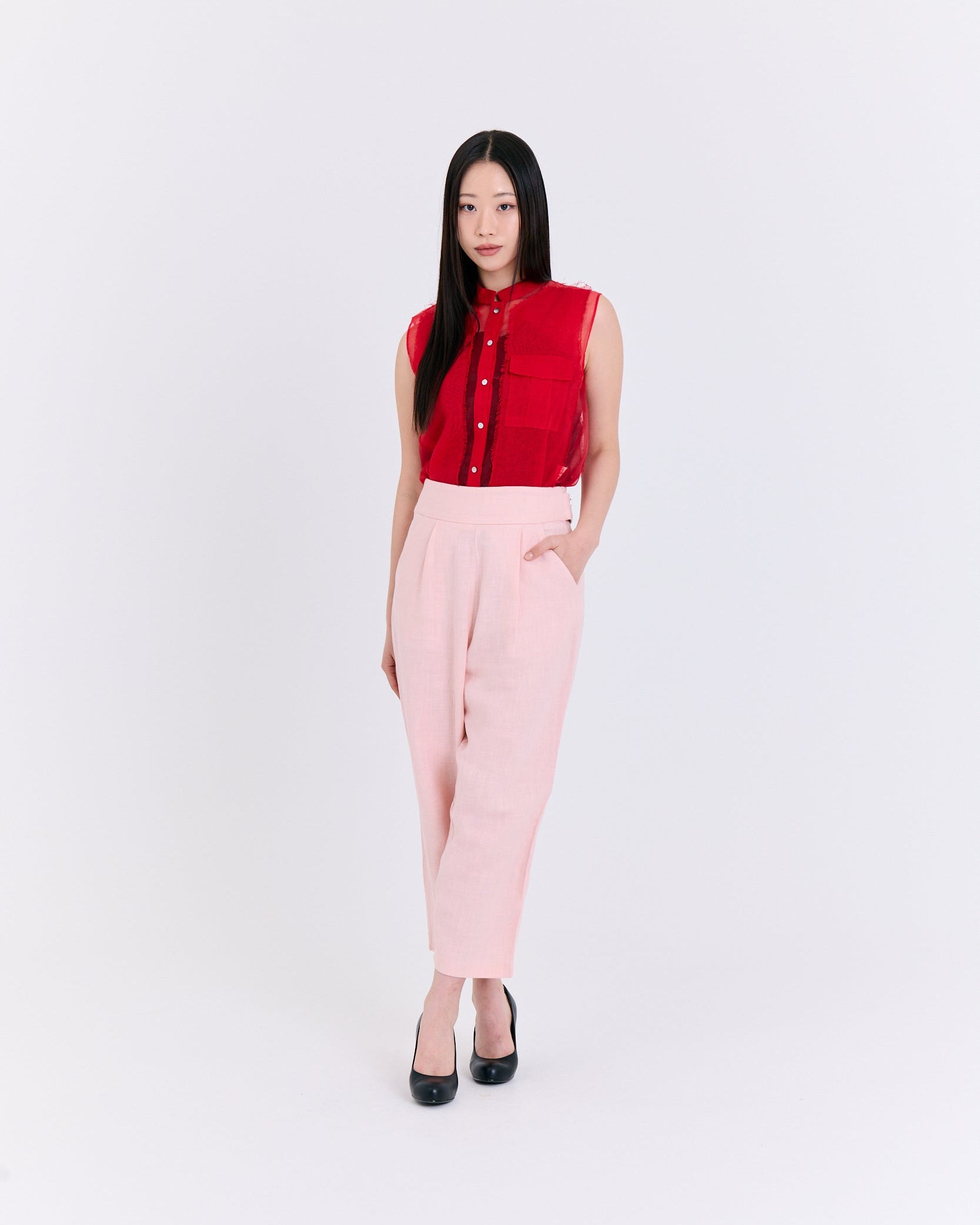 Woman wearing a red sleeveless top and pink pants on a white background